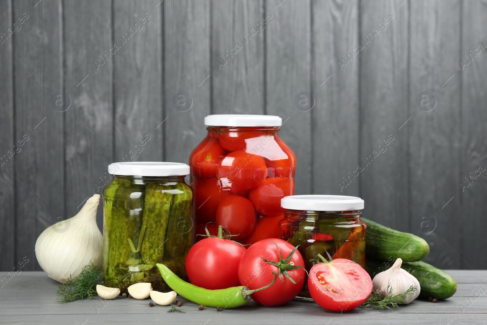 Photo of Glass jars with different pickled vegetables on grey wooden background