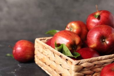 Photo of Fresh red apples and leaves in basket on dark grey table, closeup. Space for text