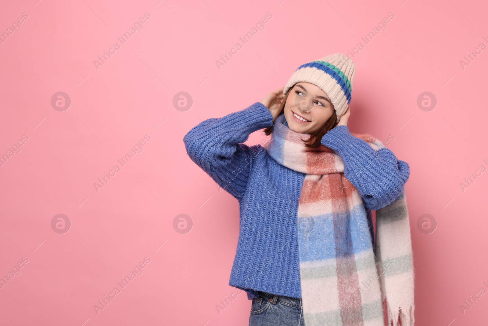 Photo of Beautiful woman in warm scarf and hat on pink background, space for text