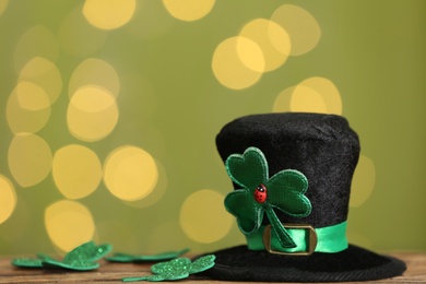 Leprechaun hat and clover leaves on wooden table against blurred lights, space for text. St Patrick's Day celebration