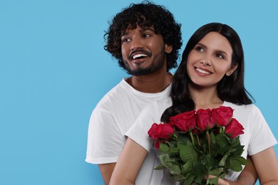 Photo of International dating. Happy couple with bouquet of roses on light blue background, space for text