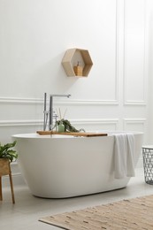 Photo of Modern ceramic bathtub and green plants near white wall in room