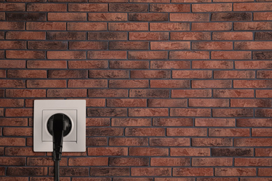 Image of Brick wall with power socket and inserted plug, space for text. Electrical supply