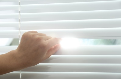 Young woman opening window blinds, closeup. Space for text