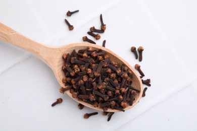 Photo of Spoon with aromatic dried clove buds on white tiled table, top view
