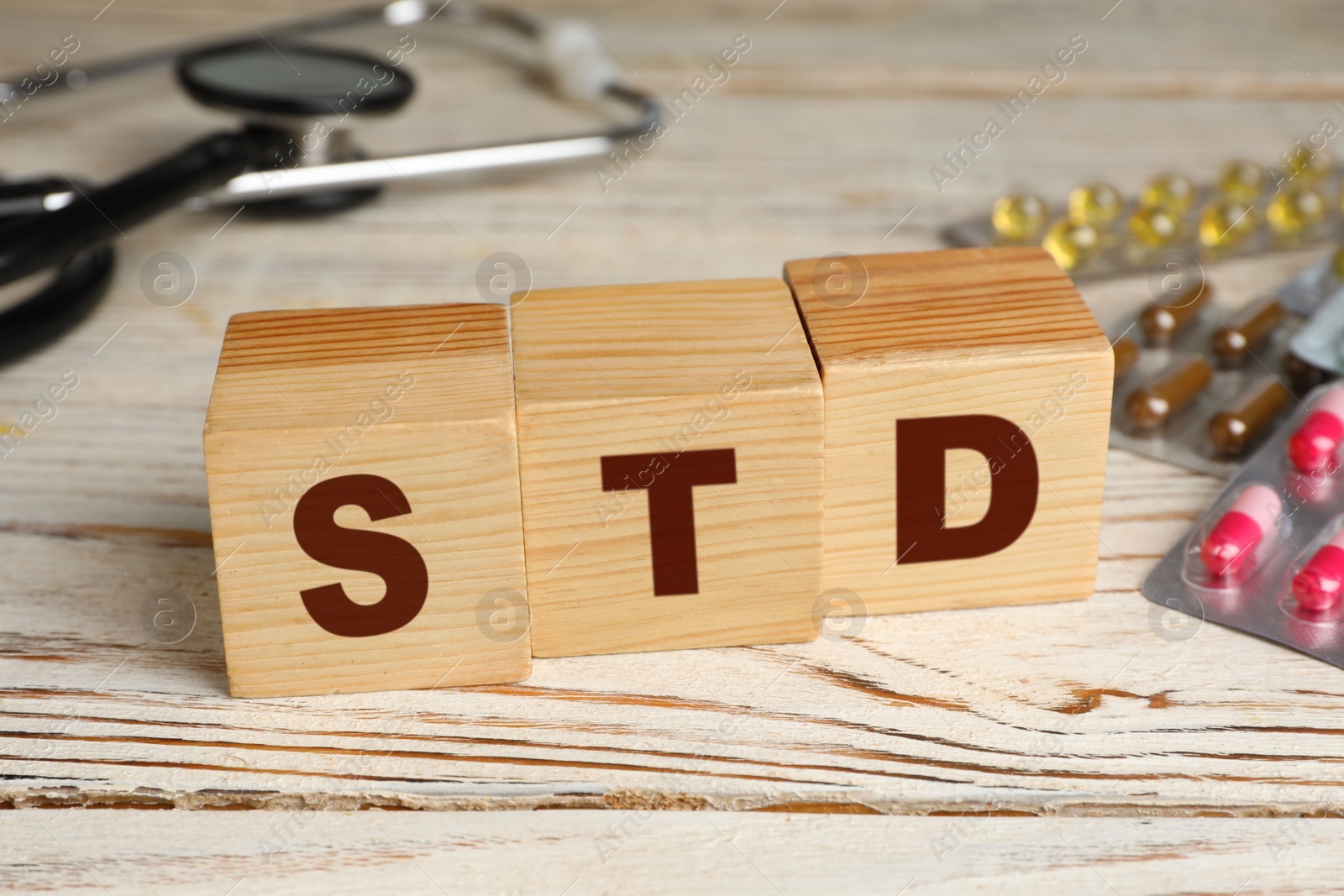 Photo of Abbreviation STD made with cubes and pills on white wooden table