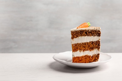 Photo of Piece of sweet carrot cake with delicious cream on white wooden table against light background. Space for text