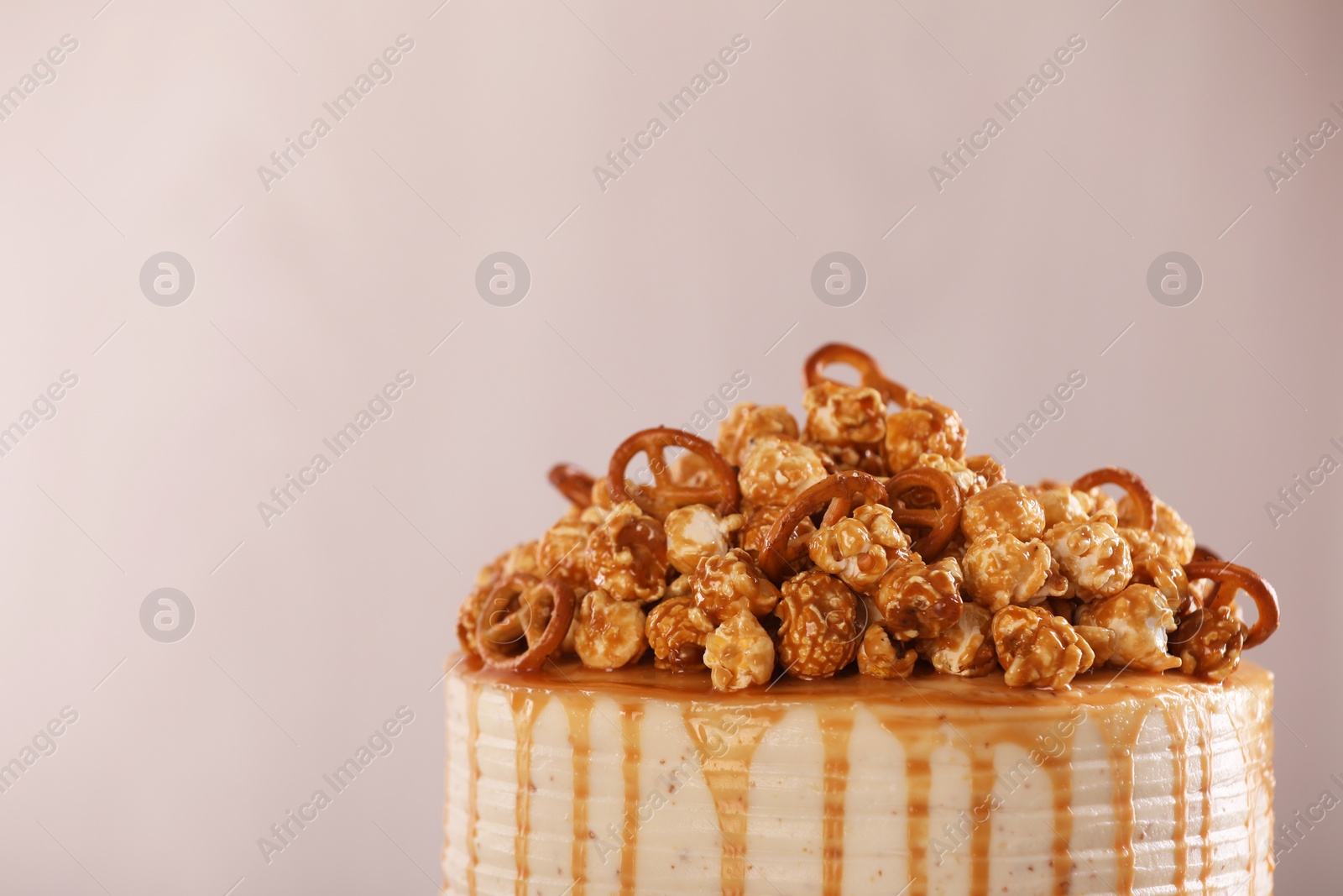 Photo of Caramel drip cake decorated with popcorn and pretzels against light background, closeup. Space for text