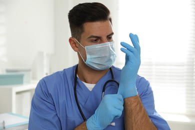 Doctor in protective mask putting on medical gloves indoors