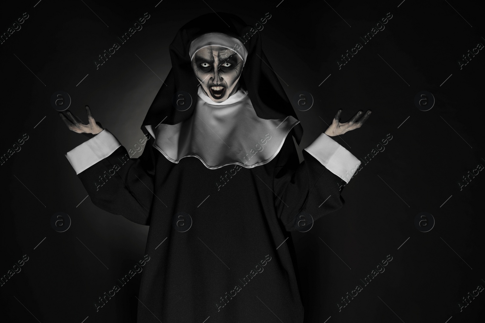 Photo of Portrait of scary devilish nun on black background. Halloween party look