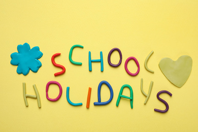 Phrase School Holidays made of modeling clay on yellow background, top view