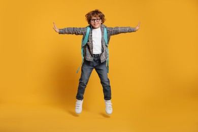 Photo of Happy schoolboy with backpack jumping on orange background
