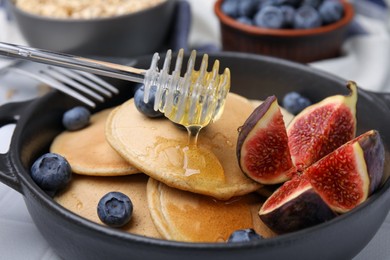 Photo of Pouring honey onto tasty oatmeal pancakes, closeup