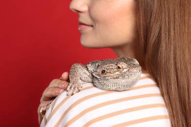 Photo of Woman with bearded lizard on red background, closeup. Exotic pet
