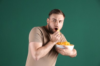 Photo of Greedy young man hiding bowl with chips on green background