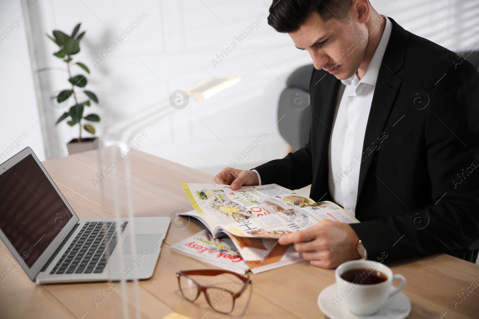 Photo of Man reading magazine at table in office