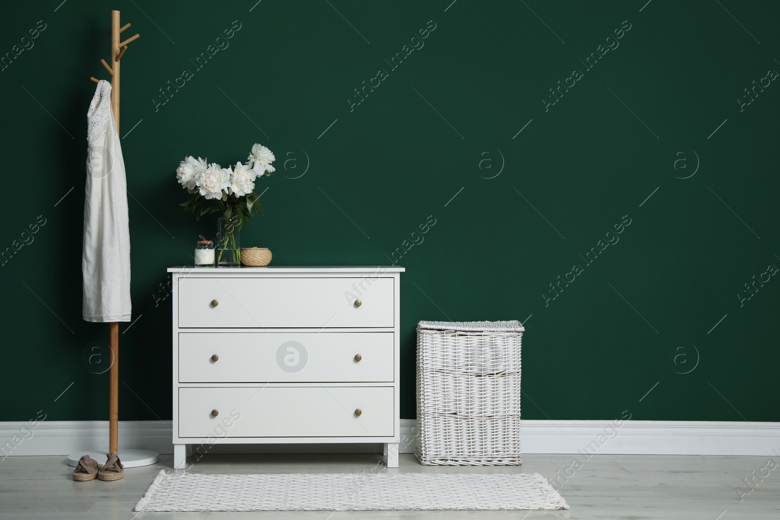 Photo of Modern white chest of drawers, coat stand and wicker basket near green wall indoors. Space for text