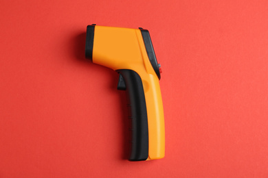 Photo of Modern non-contact infrared thermometer on red background, top view