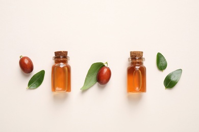 Glass bottles with jojoba oil and seeds on light background, flat lay