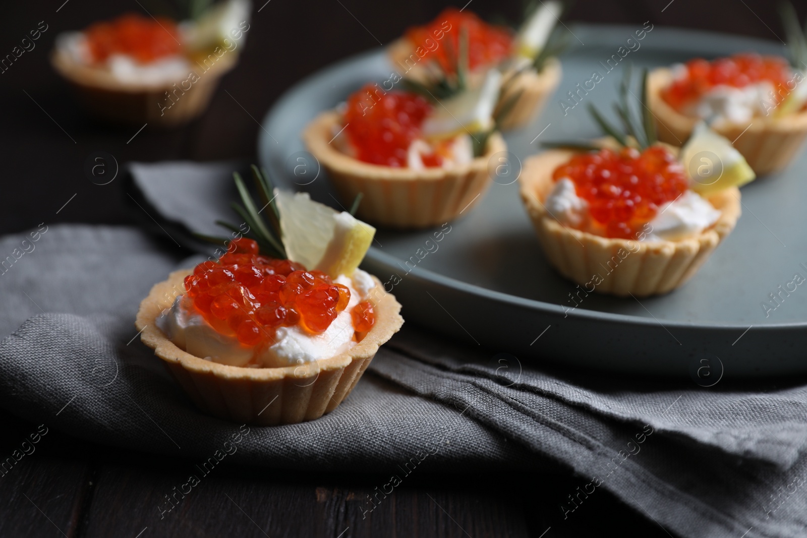 Photo of Delicious tartlets with red caviar and cream cheese served on wooden table, closeup