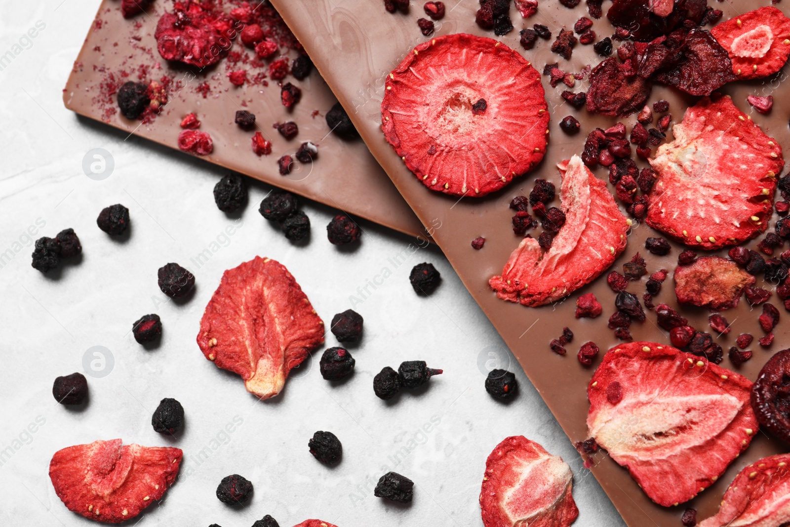 Photo of Chocolate bars with freeze dried berries on grey marble table, flat lay