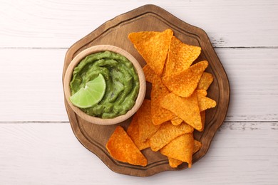 Photo of Bowl of delicious guacamole, lime and nachos chips on white wooden table, top view
