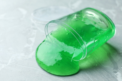 Photo of Overturned plastic container with green slime on marble background, closeup