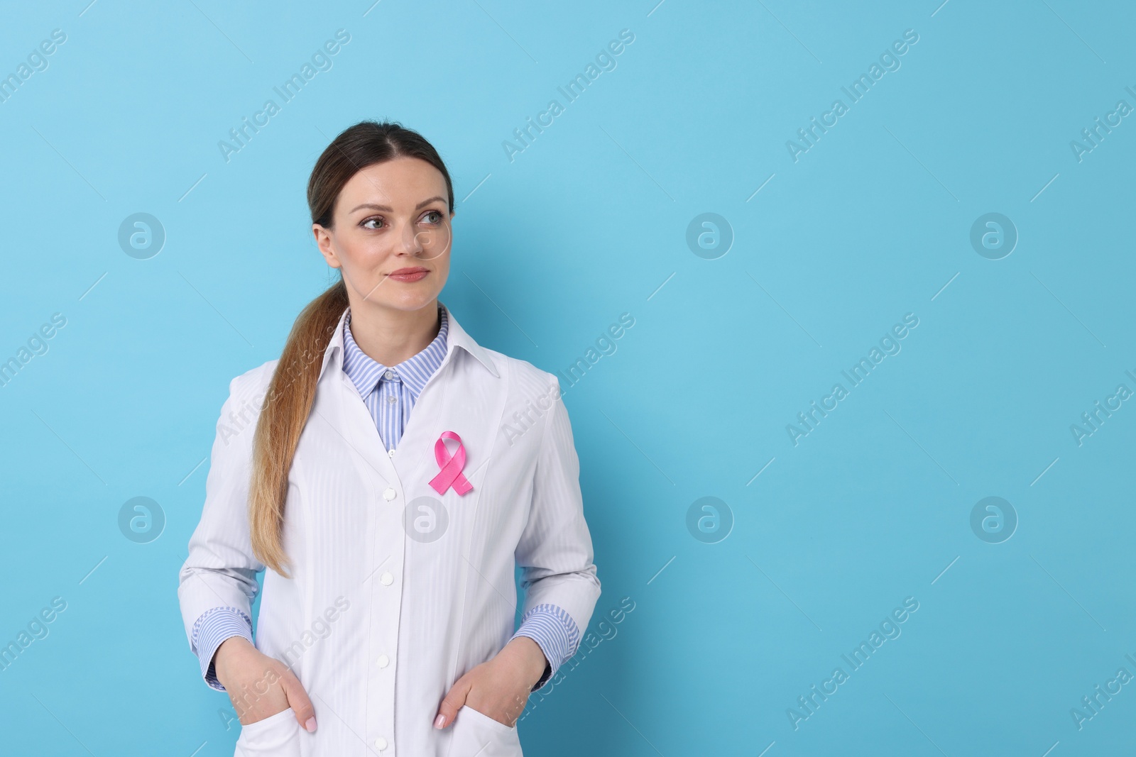 Photo of Mammologist with pink ribbon on light blue background, space for text. Breast cancer awareness