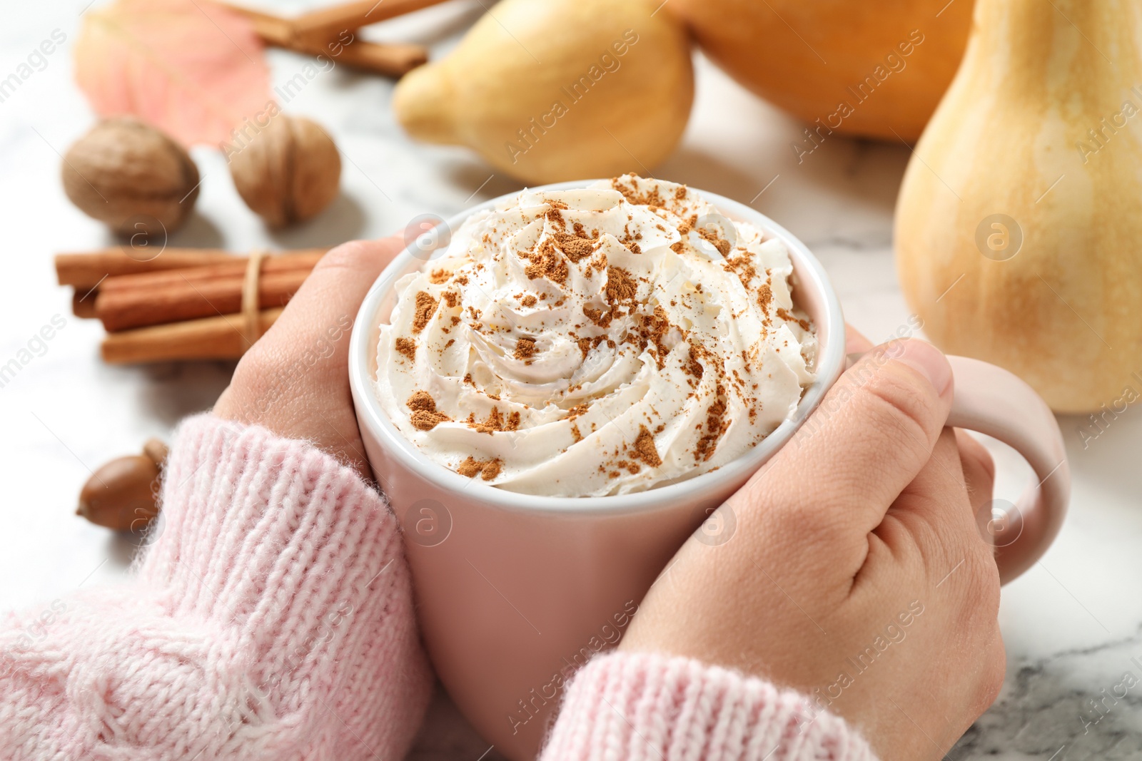 Photo of Woman holding cup with tasty pumpkin spice latte at white marble table, closeup