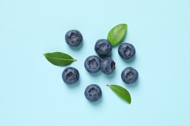 Tasty fresh blueberries with green leaves on light blue background, flat lay