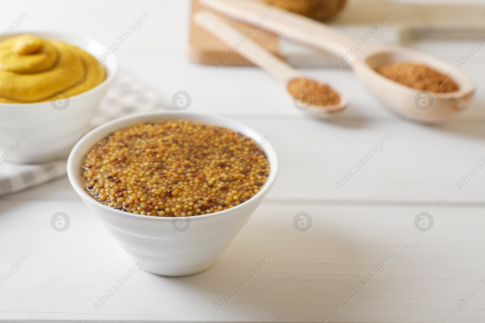 Photo of Bowls of whole grain mustard on white wooden table. Space for text