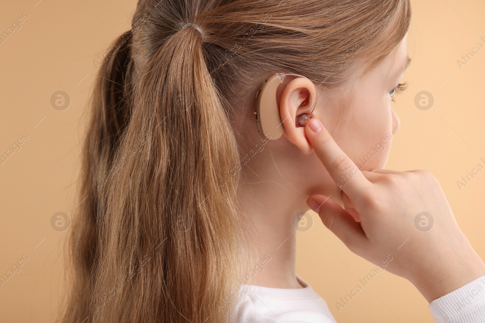 Photo of Little girl with hearing aid on pale brown background, closeup