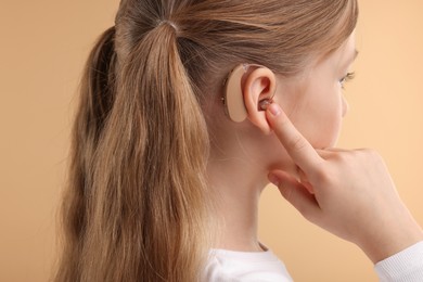 Photo of Little girl with hearing aid on pale brown background, closeup