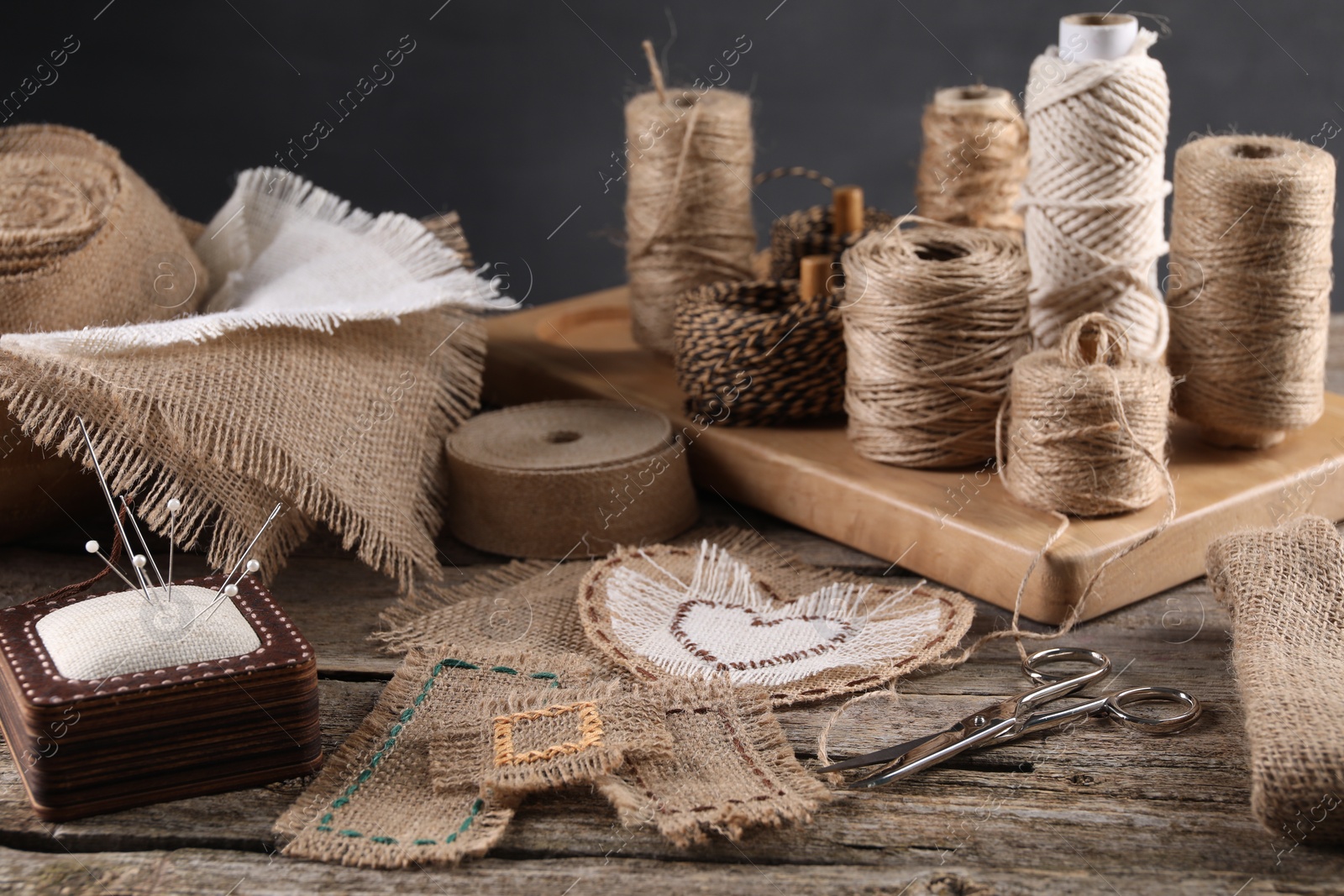 Photo of Pieces of burlap fabric, spools of twine and different sewing tools on wooden table