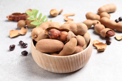 Photo of Delicious ripe tamarinds in wooden bowl on light table