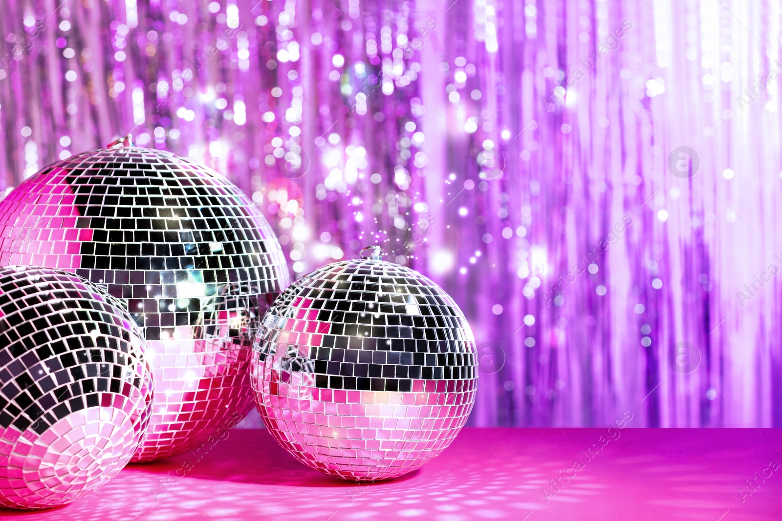Image of Shiny disco balls on table against foil party curtain, space for text. Bokeh effect