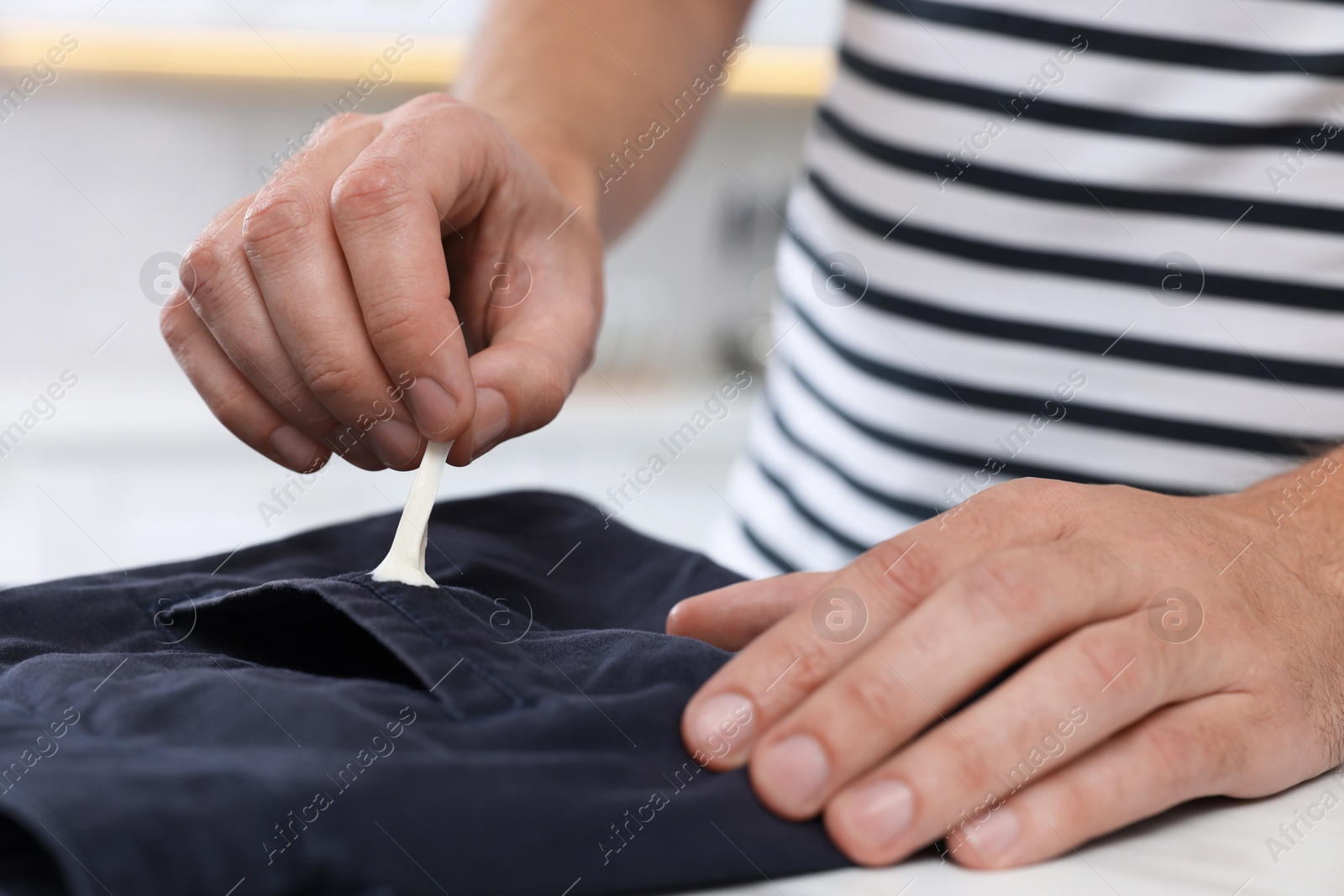 Photo of Man removing chewing gum from black jeans at white table indoors, closeup