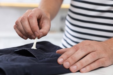 Man removing chewing gum from black jeans at white table indoors, closeup