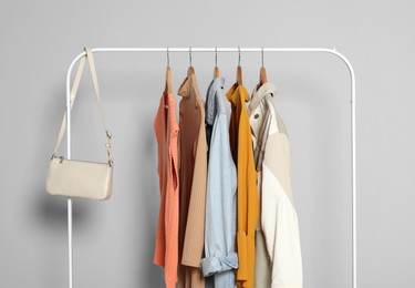 Photo of Rack with stylish women's clothes on wooden hangers and bag against light grey background