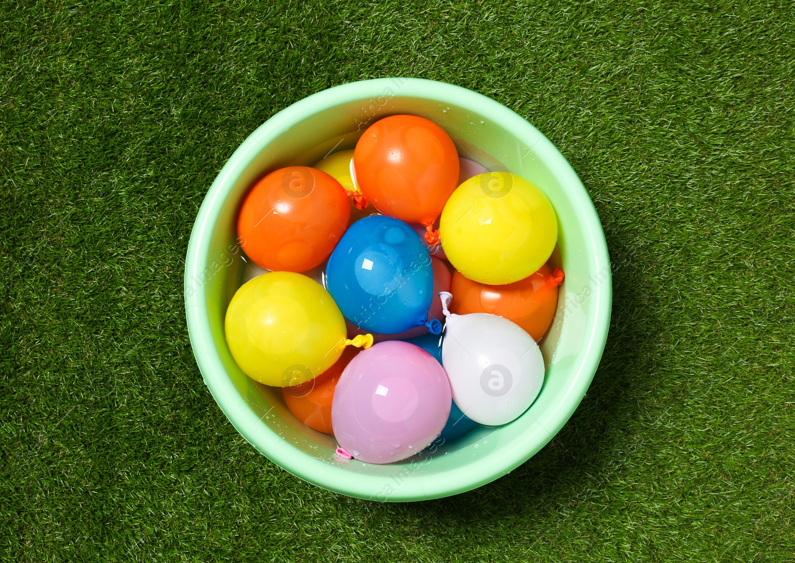 Photo of Basin full of colorful water bombs on green grass, top view