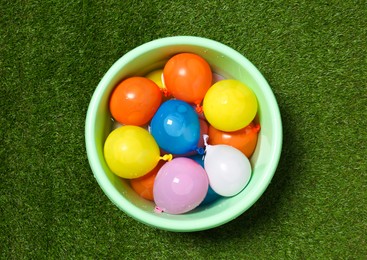 Basin full of colorful water bombs on green grass, top view