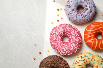 Yummy donuts with sprinkles on light grey table, top view. Space for text