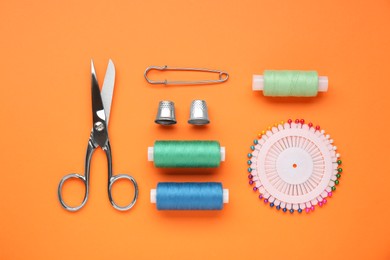 Flat lay composition with thimbles and different sewing tools on orange background
