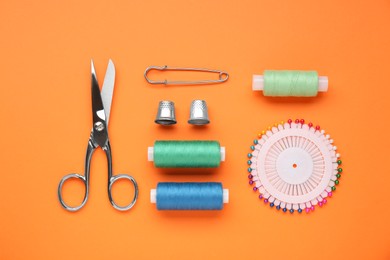 Photo of Flat lay composition with thimbles and different sewing tools on orange background