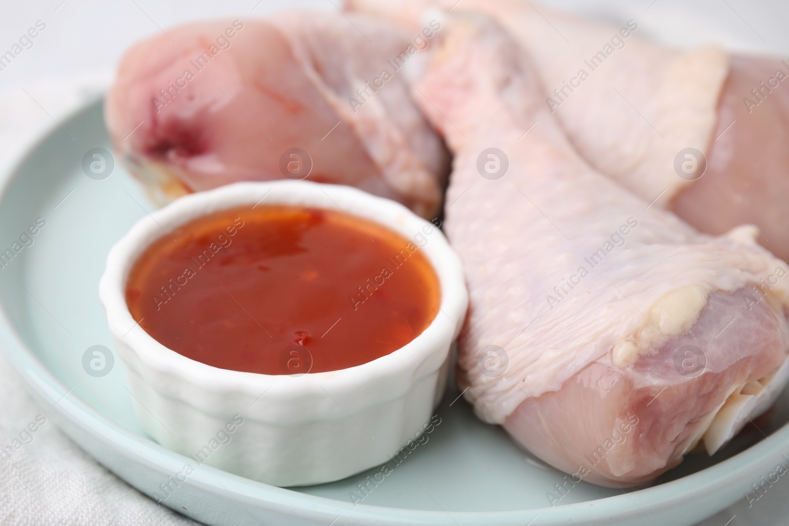 Photo of Fresh marinade and raw chicken drumsticks on table, closeup