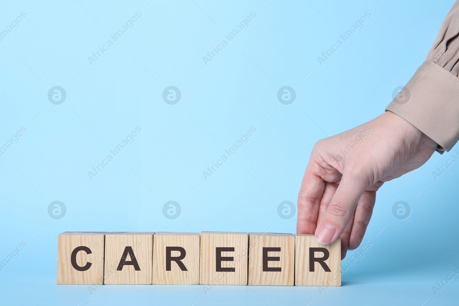 Photo of Woman making word CAREER with wooden cubes on light blue background, closeup. Space for text