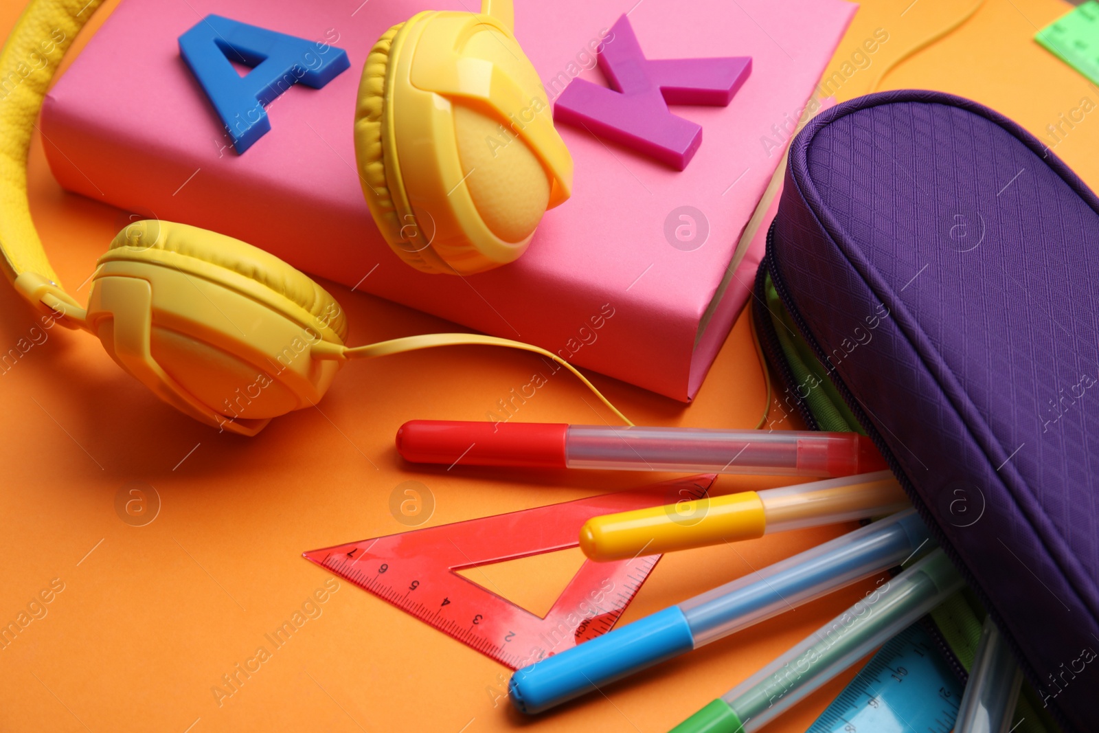 Photo of Book, headphones and stationery on orange background, closeup