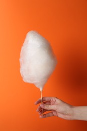 Photo of Woman holding sweet cotton candy on orange background, closeup