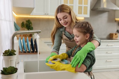 Photo of Mother and daughter in protective gloves washing plate above sink in kitchen