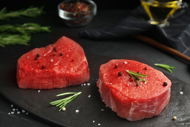 Photo of Fresh raw beef cut with spices on black table, closeup